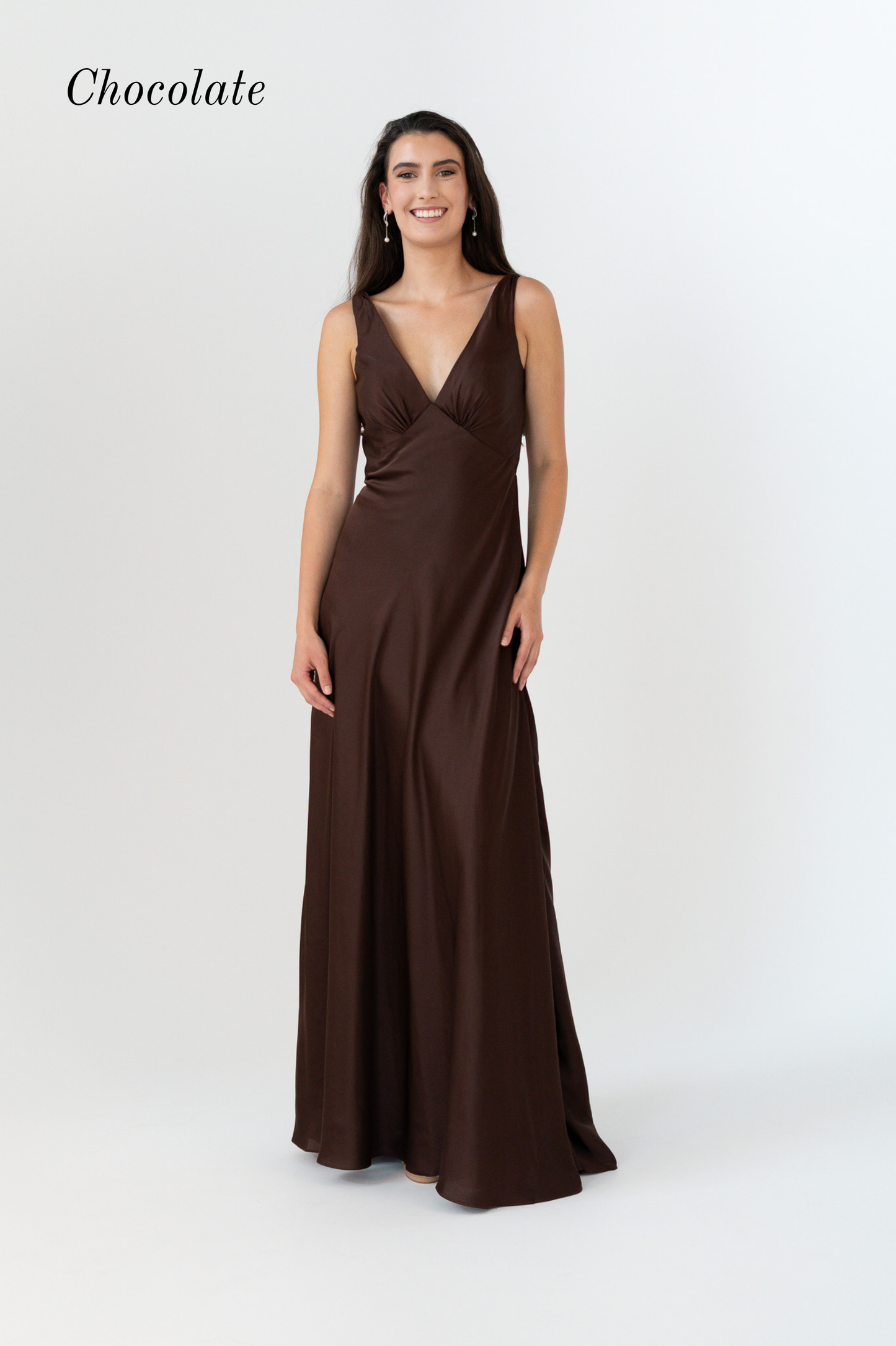 A woman modeling a floor-length chocolate brown satin gown with a deep V-neckline and sleeveless design, set against a plain light gray studio background with the word 'Chocolate' in the top left.