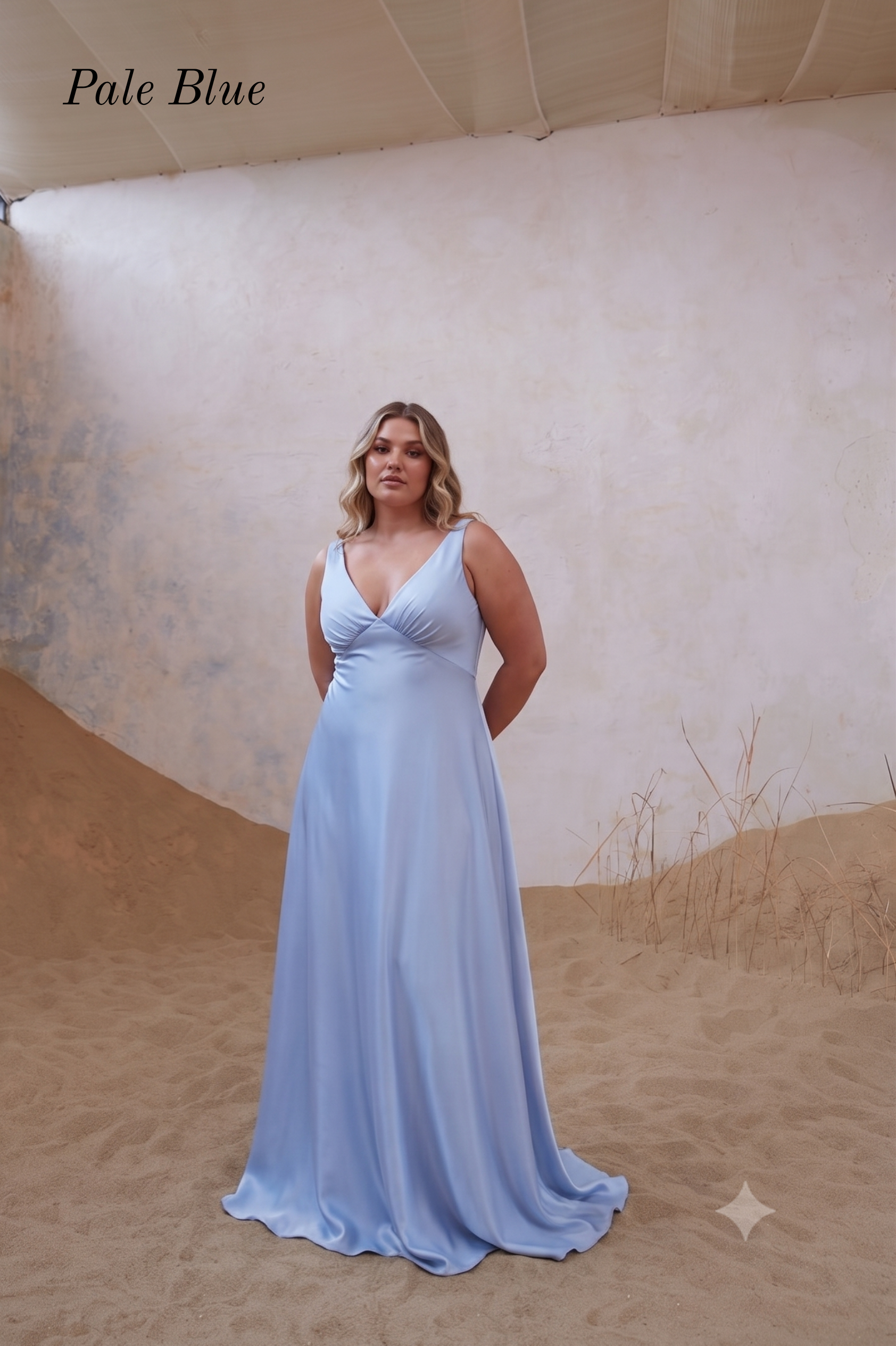 A woman modeling a sleeveless pale blue floor-length gown with a deep V-neckline, standing in a sandy studio setup with a textured beige backdrop. The words 'Pale Blue' appear in the upper left corner.