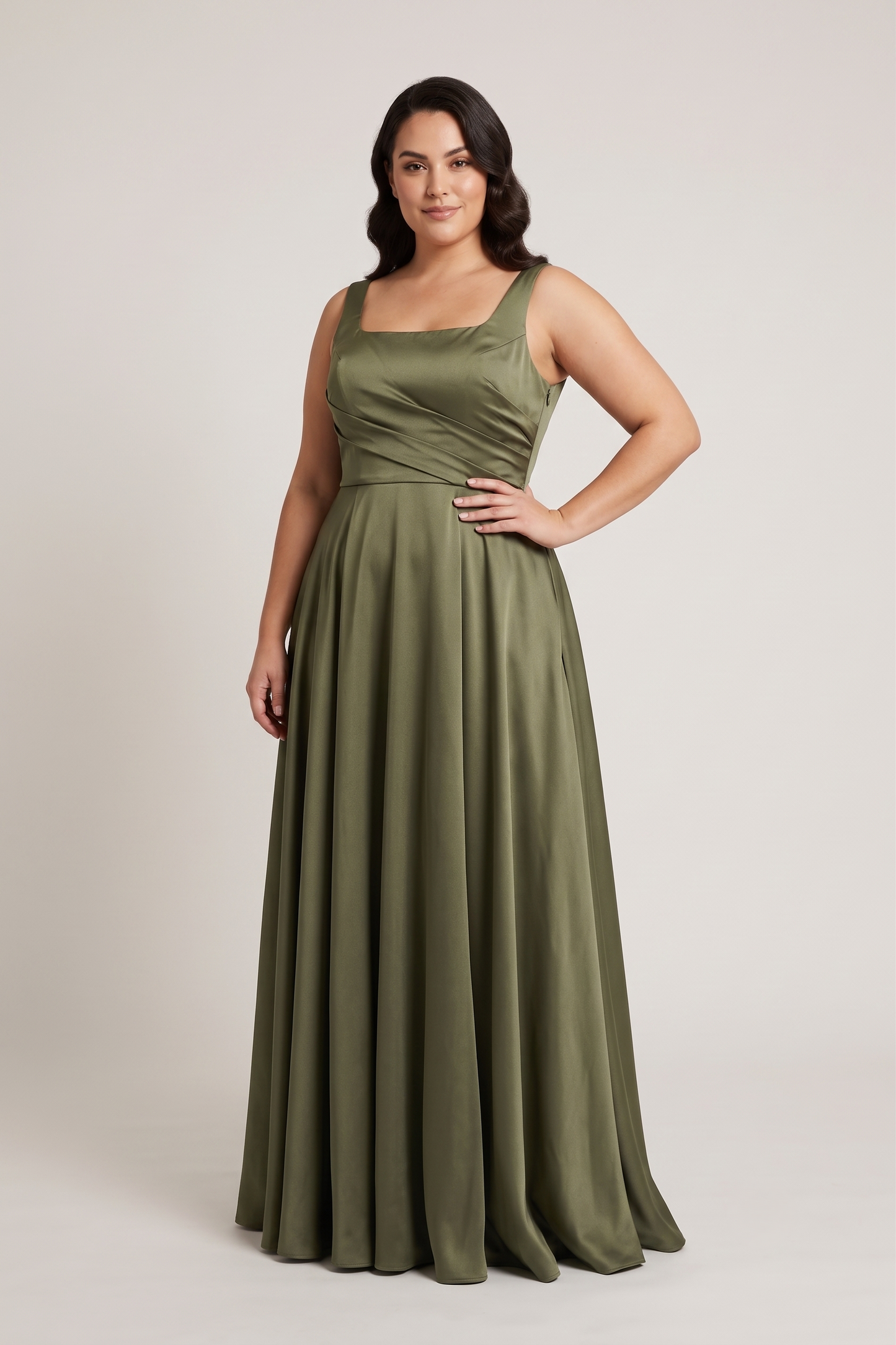 A woman modeling a floor-length olive green sleeveless gown with a square neckline and a flowing skirt, photographed against a plain light gray studio background.