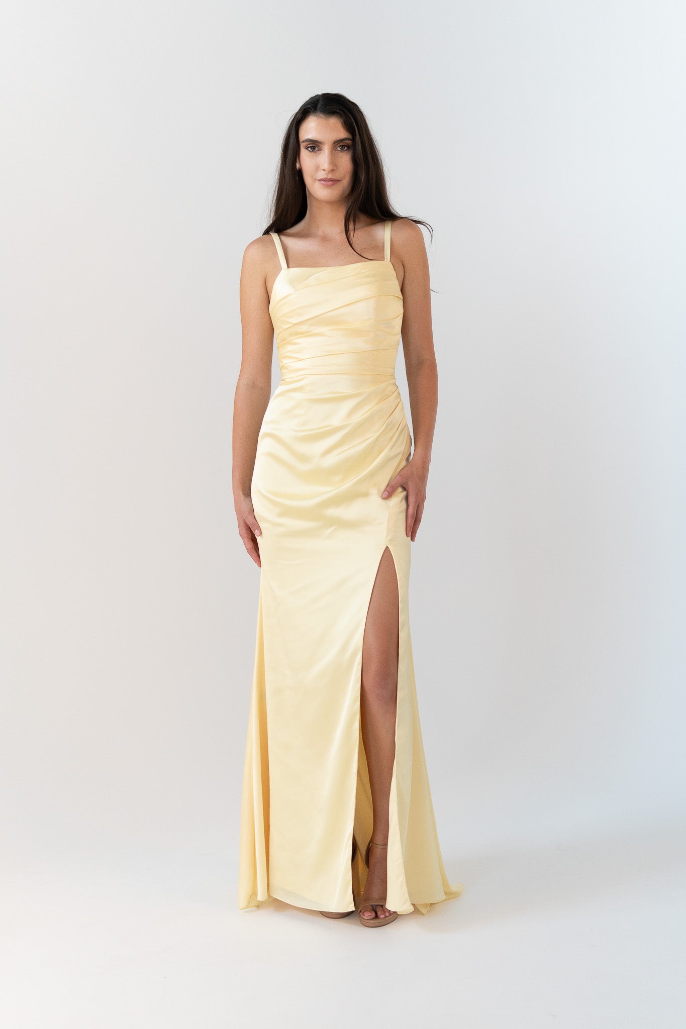 Woman wearing a light yellow evening gown with a slit on a white background