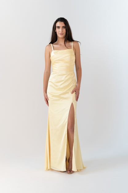 Woman wearing a light yellow evening gown with a slit on a white background