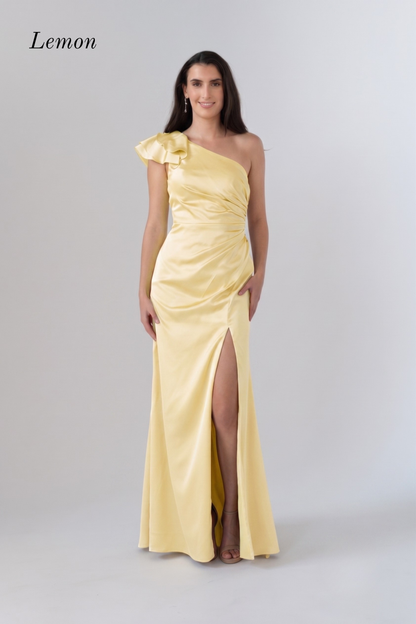 A woman modeling a lemon yellow one-shoulder satin evening gown with a ruffled shoulder detail, ruched bodice, and high front slit, set against a light gray studio background with the word 'Lemon' in the top left.