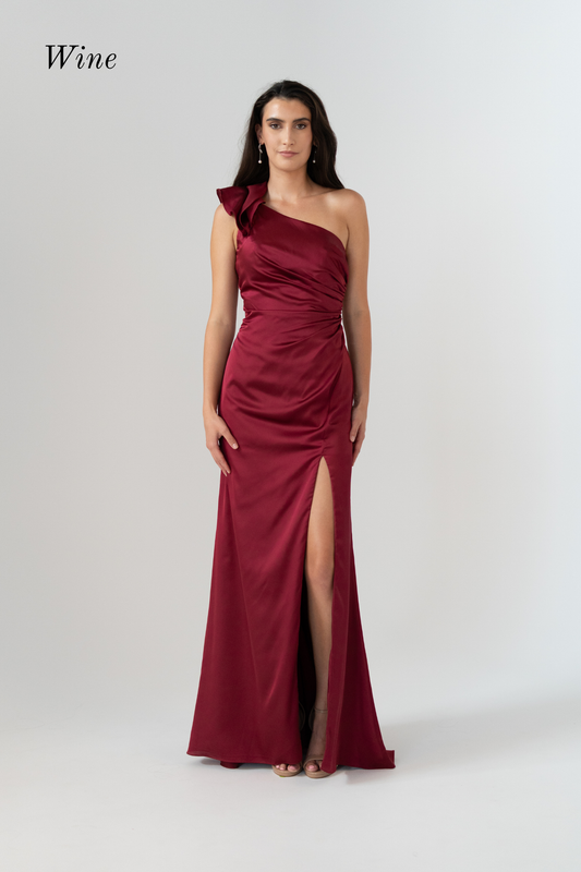 A woman modeling a wine-red satin one-shoulder evening gown with a high thigh slit, photographed against a light gray studio background. The word 'Wine' appears in the upper left corner.