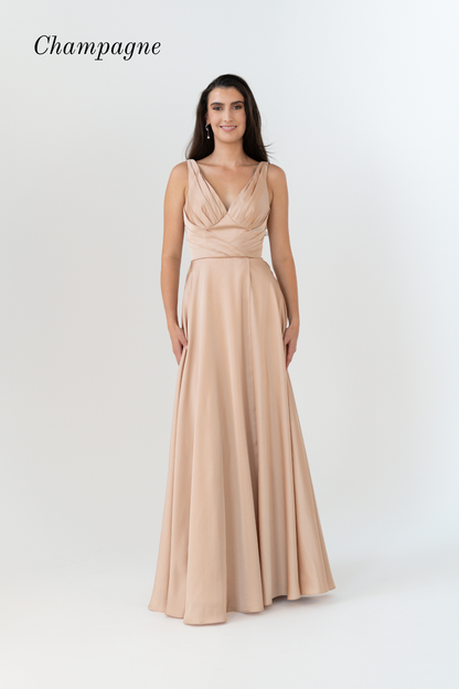 A woman modeling a floor-length champagne gown with a draped, wrap-style bodice and flowing skirt against a light gray studio background. The word 'Champagne' appears in the upper left corner.