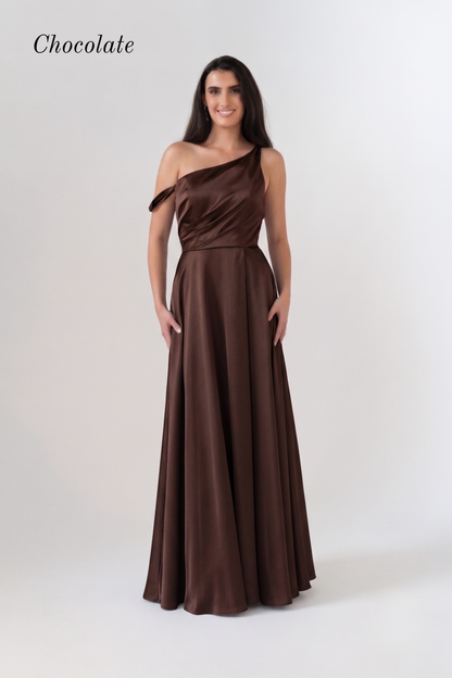 A woman modeling a chocolate brown one-shoulder floor-length gown against a plain light gray studio background. The word 'Chocolate' appears in the upper left corner.