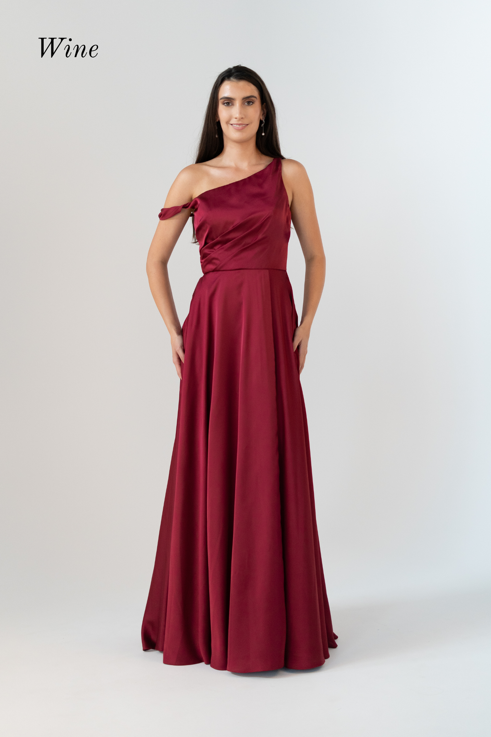 A woman modeling a floor-length one-shoulder gown in a deep wine red color, standing against a light gray studio background. The word 'Wine' appears in the upper left corner.