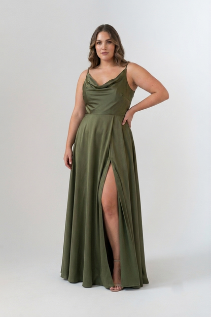 A woman modeling a floor-length olive green satin gown with a draped neckline, thin straps, and a high thigh slit, photographed against a light gray studio background.