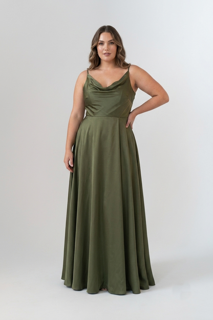 A woman modeling a floor-length olive green sleeveless gown with thin straps, a draped neckline, and a fitted waist with a full flowing skirt, photographed against a light gray studio background.