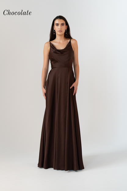 A woman modeling a floor-length chocolate brown satin gown with a cowl neckline and thin spaghetti straps against a light gray studio background. The word 'Chocolate' appears in the upper left corner.