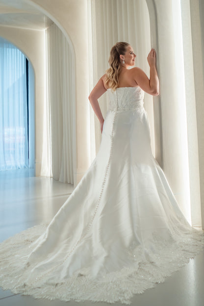 Woman in a white wedding dress standing in a bright room with large windows.