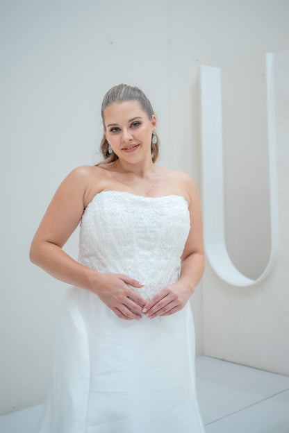 Woman in a white strapless dress standing against a plain background