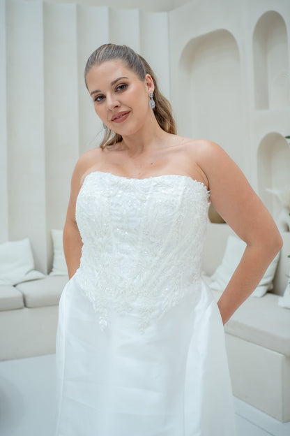 Woman in a strapless white wedding dress standing in a modern indoor setting.