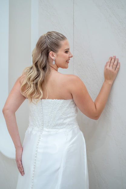 Woman in a white strapless dress standing against a plain background