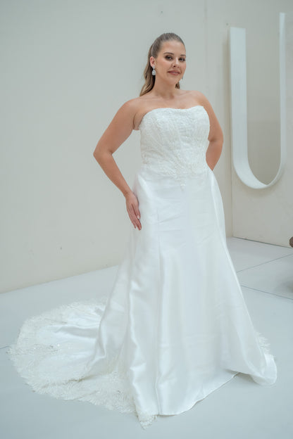 Woman wearing a white strapless wedding dress with a long train against a plain background