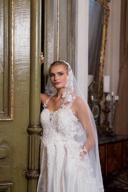 Woman in a white wedding dress with a veil standing in a room with ornate decor.