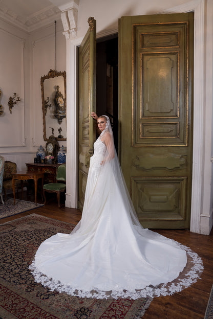 Woman in a white wedding dress standing in a room with ornate decor.