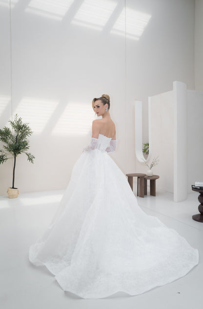 Woman in a white wedding dress standing in a minimalistic room with white walls and a plant.