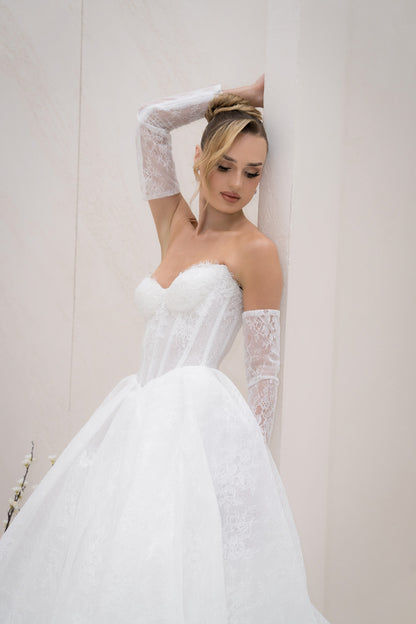 Woman in a white wedding dress with lace gloves against a plain background