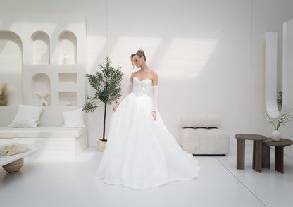 Woman in a white wedding dress standing in a modern, minimalistic room with white walls and furniture