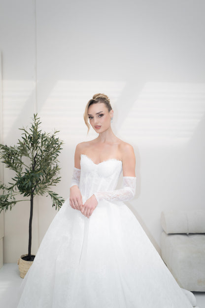 Woman in a white wedding dress sitting indoors with a plant in the background