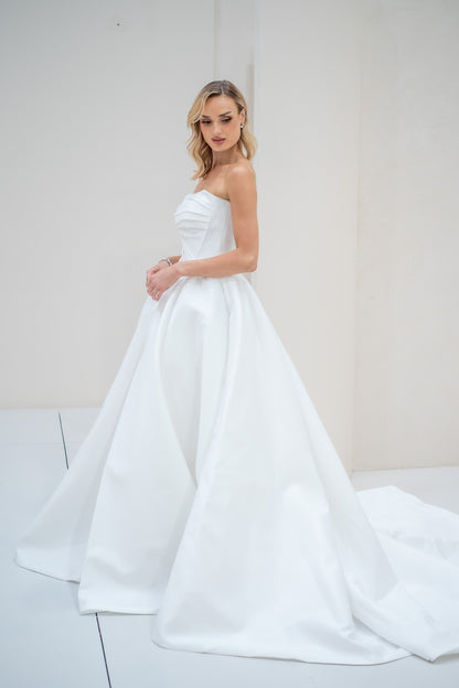 Woman wearing a strapless white wedding dress against a plain background
