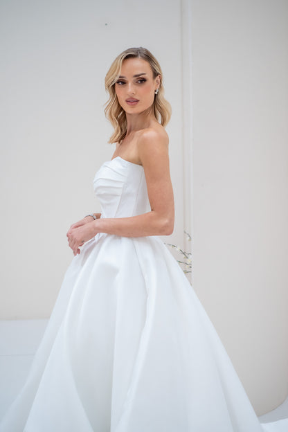Woman wearing a strapless white wedding dress against a plain background