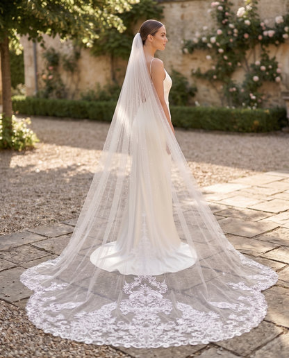 Bride in a white wedding dress with a long veil standing outdoors on a stone path.