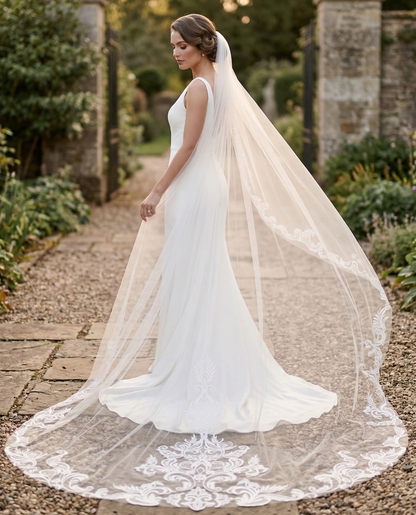 Bride in a white wedding dress with a long veil standing in a garden setting.