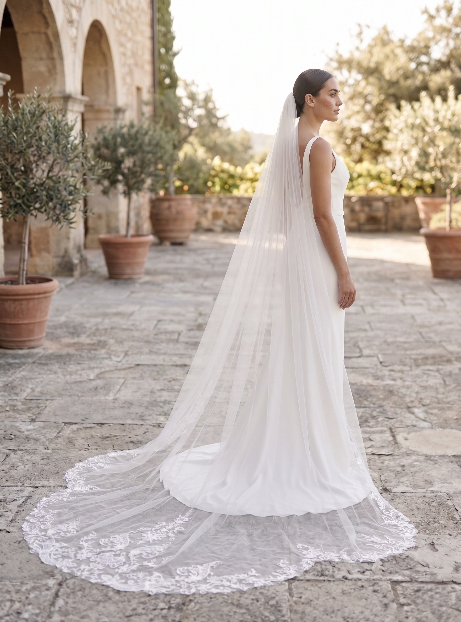 Woman in a white wedding dress with a long veil standing in an outdoor setting.