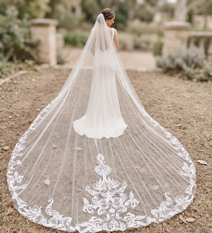 Bride wearing a long, elegant wedding veil with intricate lace details outdoors.