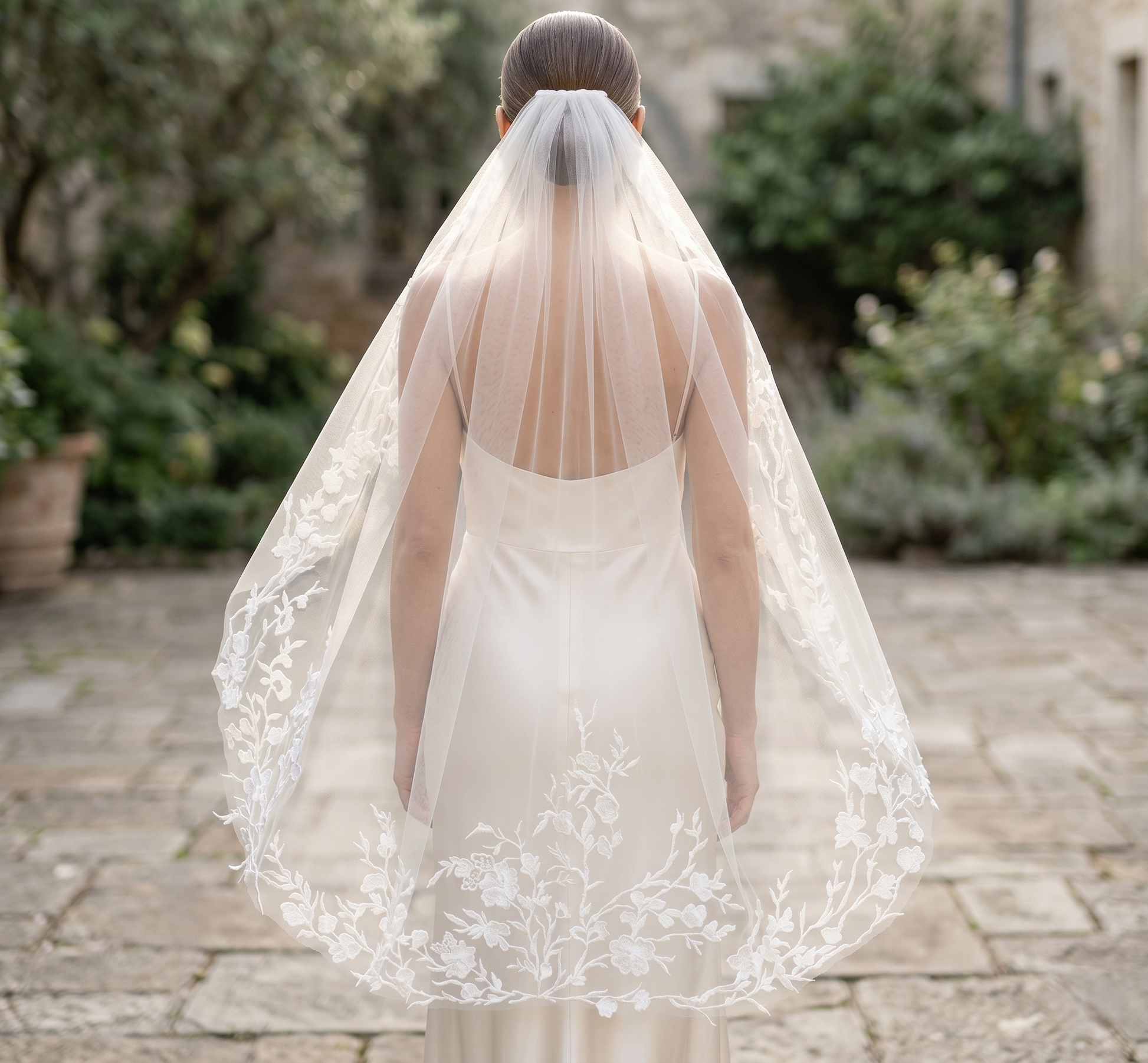Bride wearing a long, lace-trimmed veil outdoors.