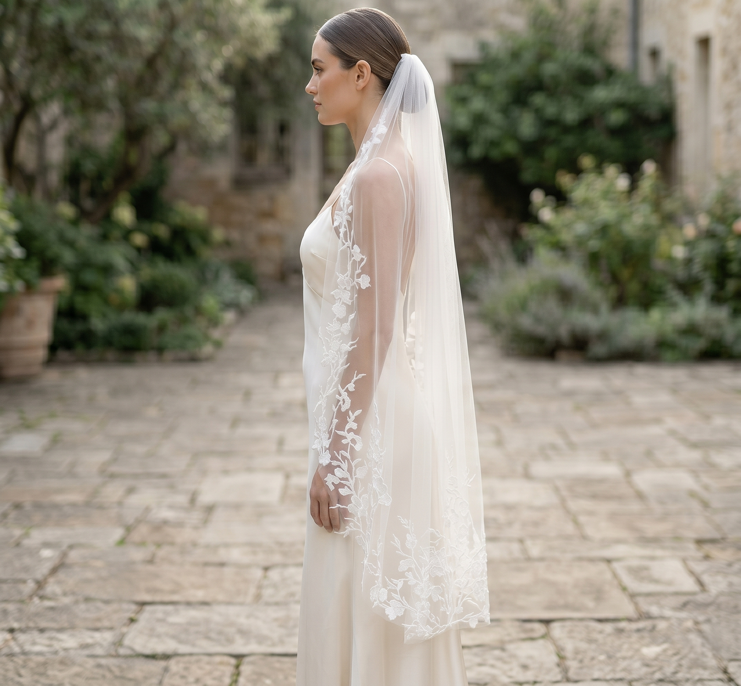 Woman wearing a white lace wedding dress and veil in an outdoor setting.