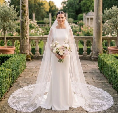Bride in a white wedding dress with a long veil holding a bouquet in an outdoor garden setting.