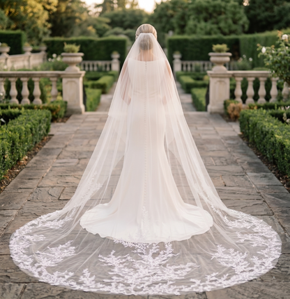 Person wearing a long, elegant wedding veil in an outdoor setting with greenery.