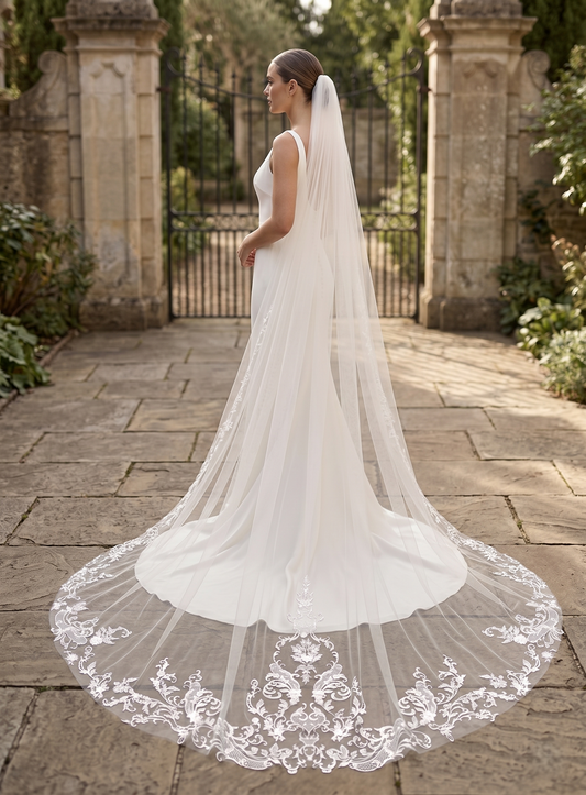 Bride in a white wedding dress with a long veil standing outdoors.
