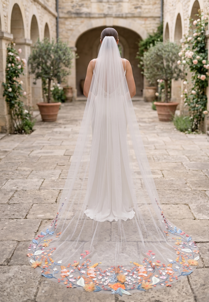 Person wearing a long wedding veil with colorful accents in an outdoor setting.