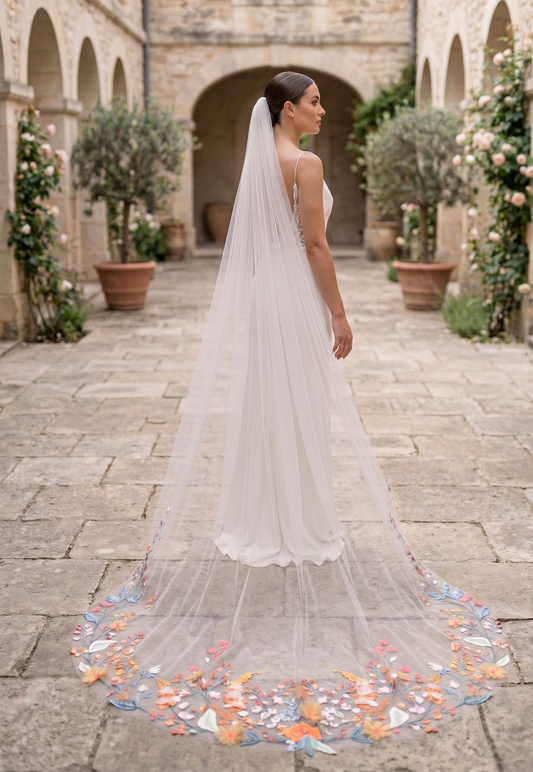 Bride in a white wedding dress with a long veil standing in an outdoor setting with stone pavement and decorative plants.