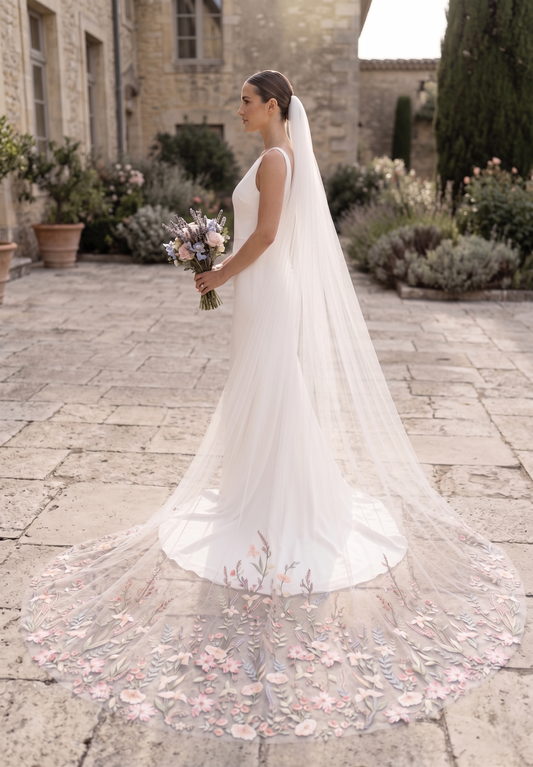 Bride in a white wedding dress with a long veil standing in an outdoor setting.