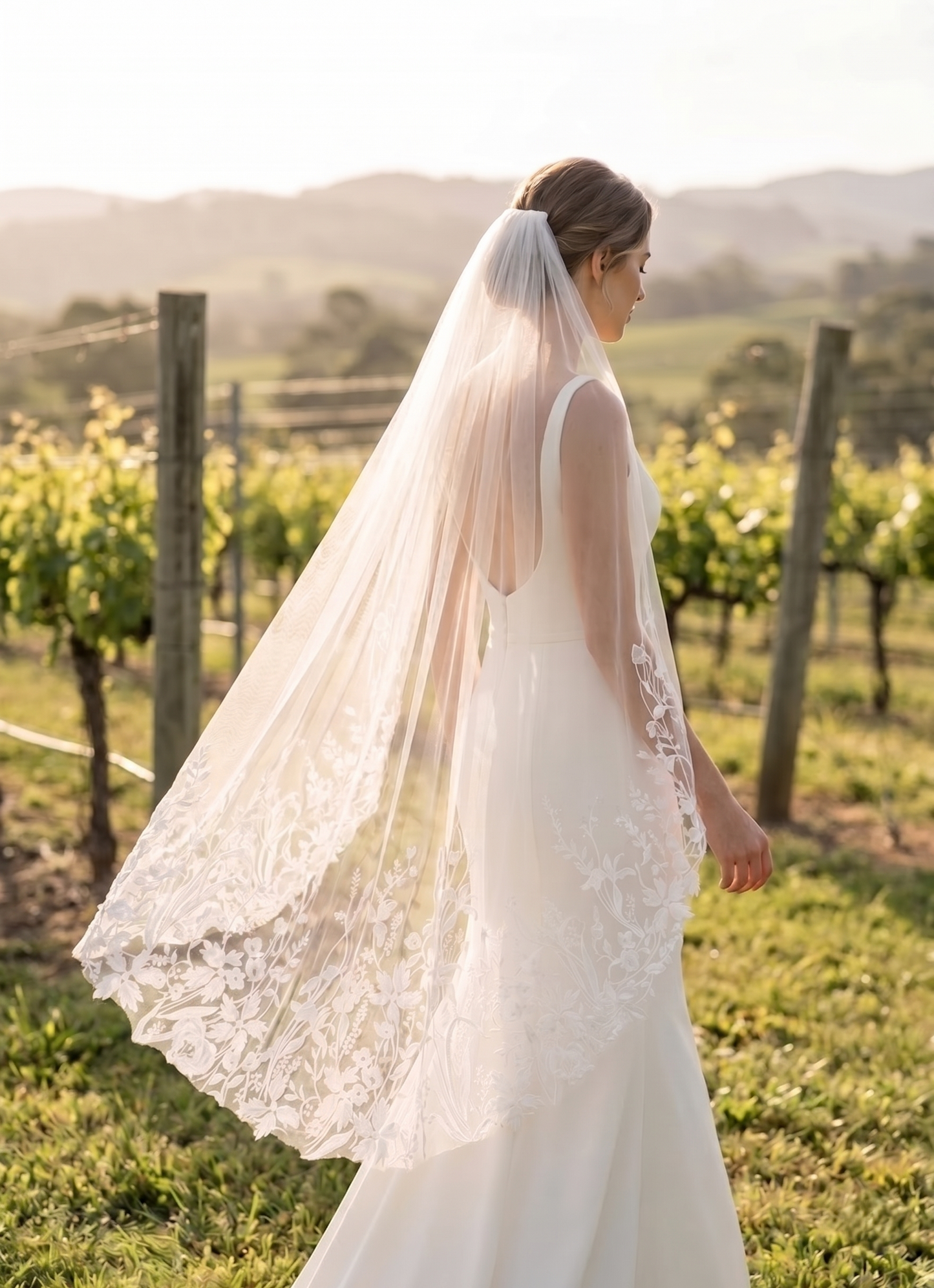 Woman in a wedding dress with a long veil standing in a vineyard.