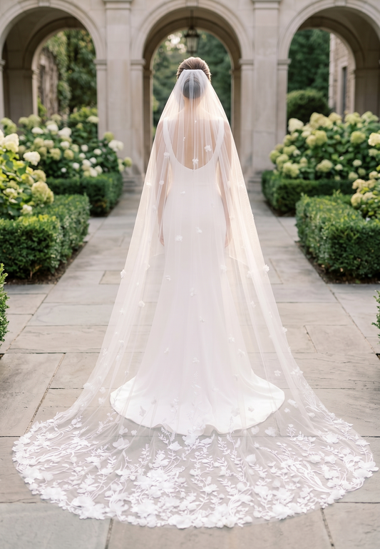 White wedding dress with a long train and veil in an outdoor setting with arches and greenery.