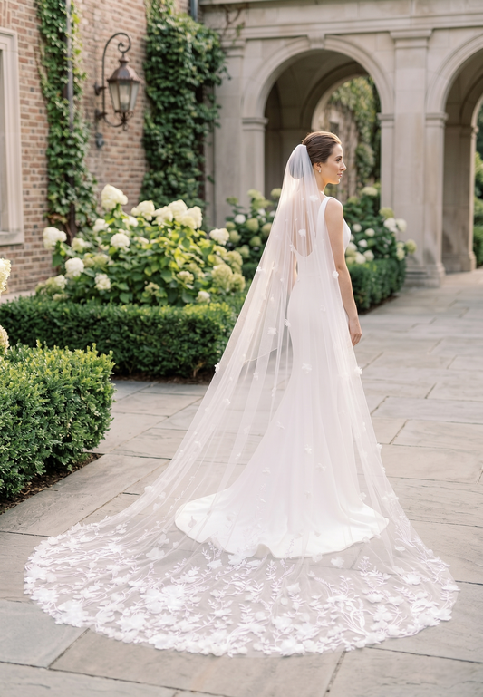 Bride in a white wedding dress with a long veil standing in an elegant outdoor setting.