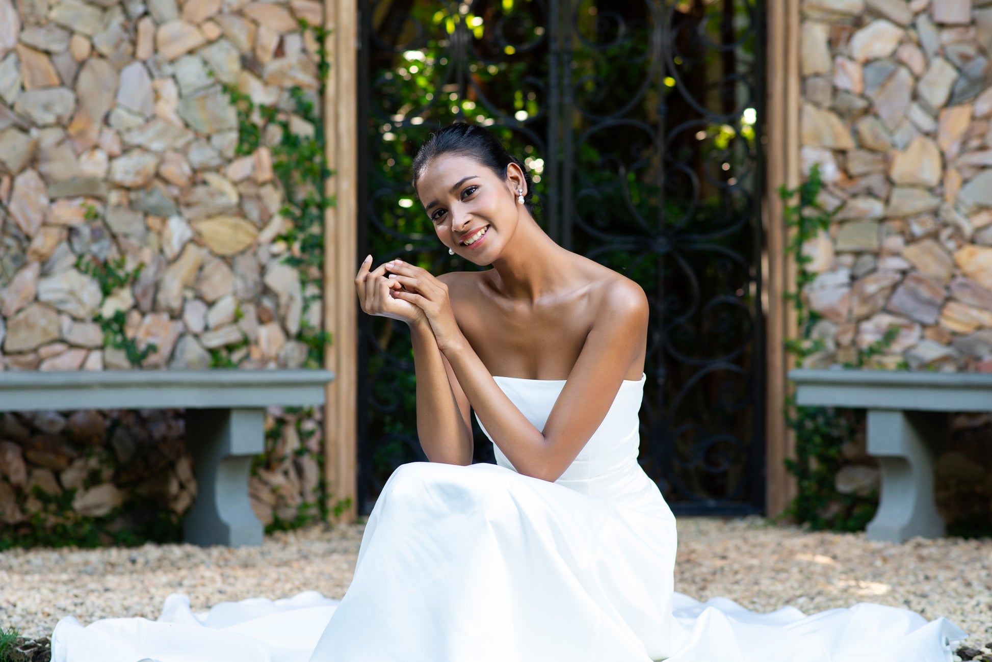 Bride in strapless satin gown seated at stone courtyard