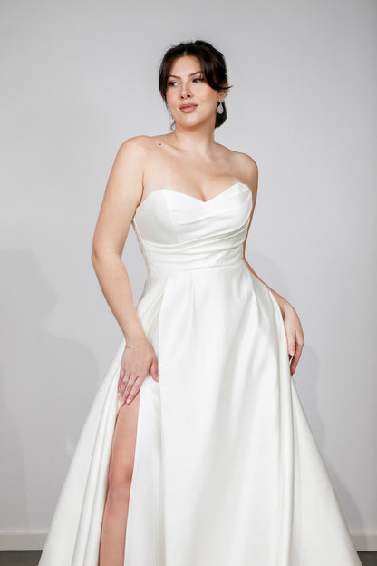 Woman wearing a white strapless gown with a slit on a plain background