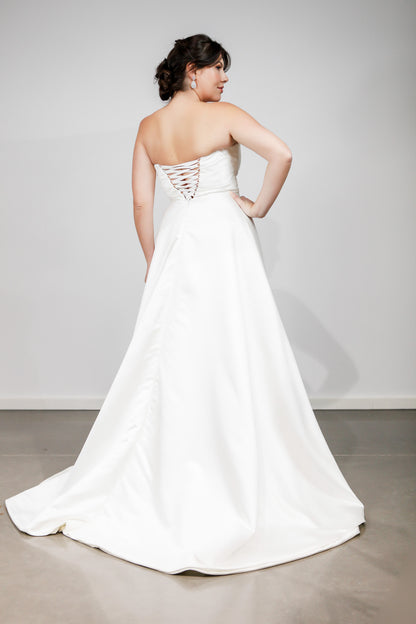 Woman wearing a strapless white wedding dress with a plain background