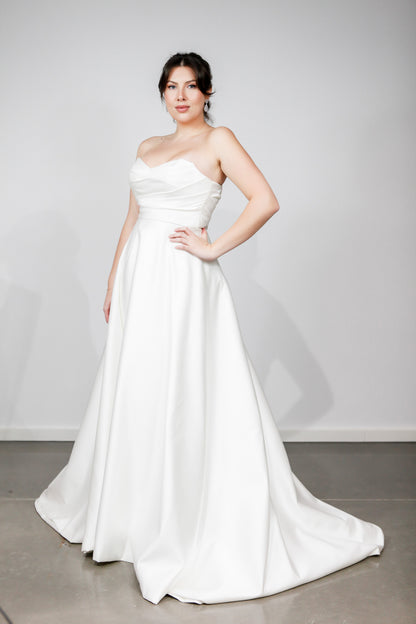 Woman wearing a white strapless gown against a plain background