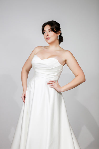 Woman wearing a white strapless gown against a gray background