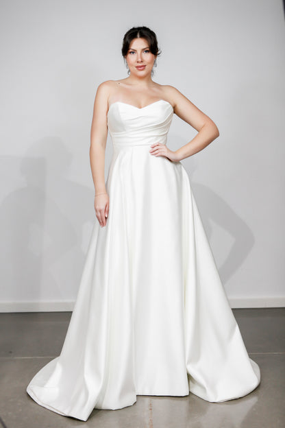 Woman wearing a strapless white wedding dress against a plain background