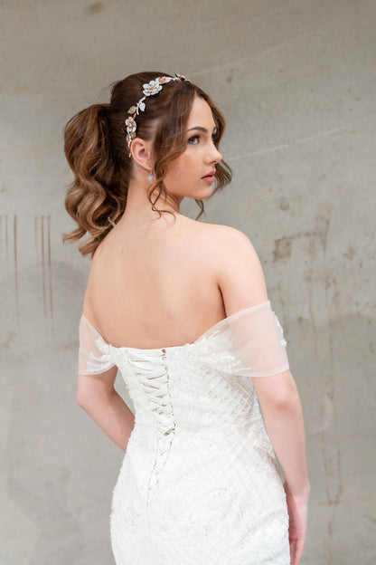 Woman in a white wedding dress with sheer sleeves against a plain background