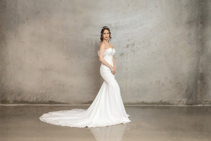 Woman in a white wedding dress standing against a plain wall.