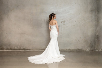 Woman in a white wedding dress standing against a plain wall.